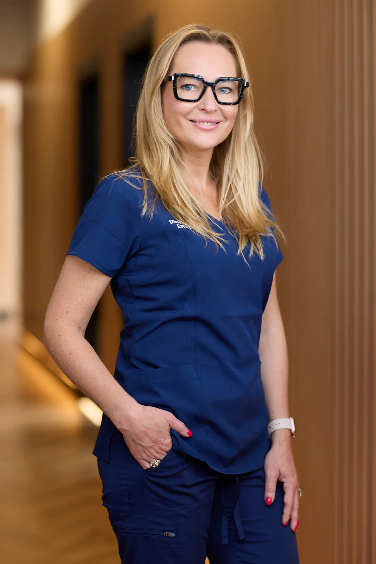 business headshot for dental practice. Woman wears branded scrubs and smiles at the camera in her place of work