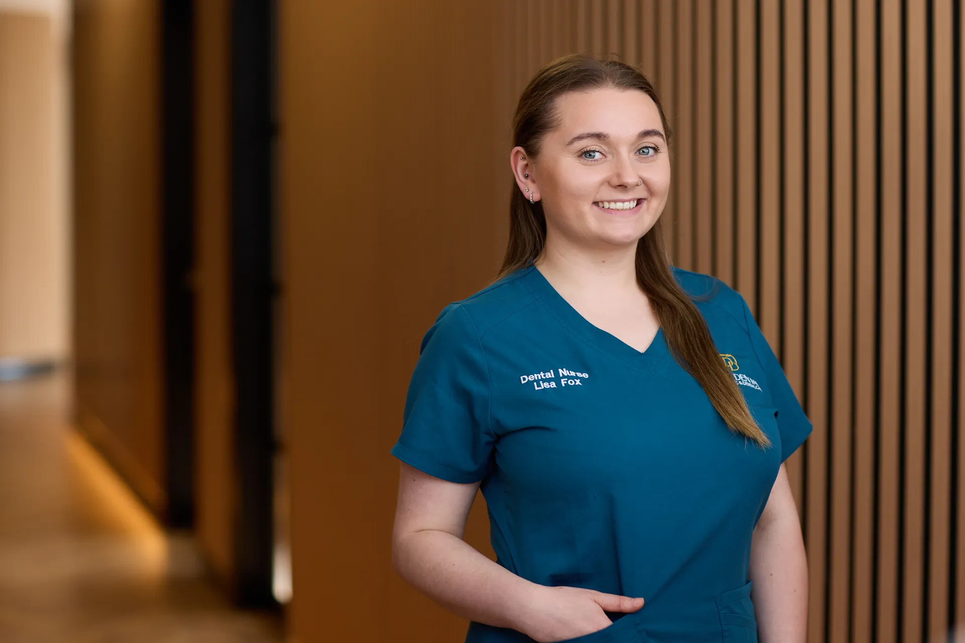 business headshot for dental practice. Woman wears branded scrubs and smiles at the camera in her place of work