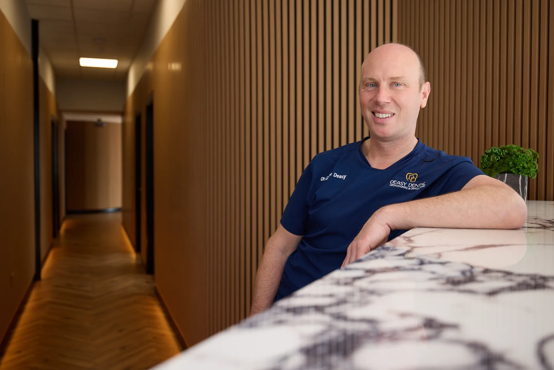 business headshot for dental practice. Man wears branded scrubs and smiles at the camera in his place of work