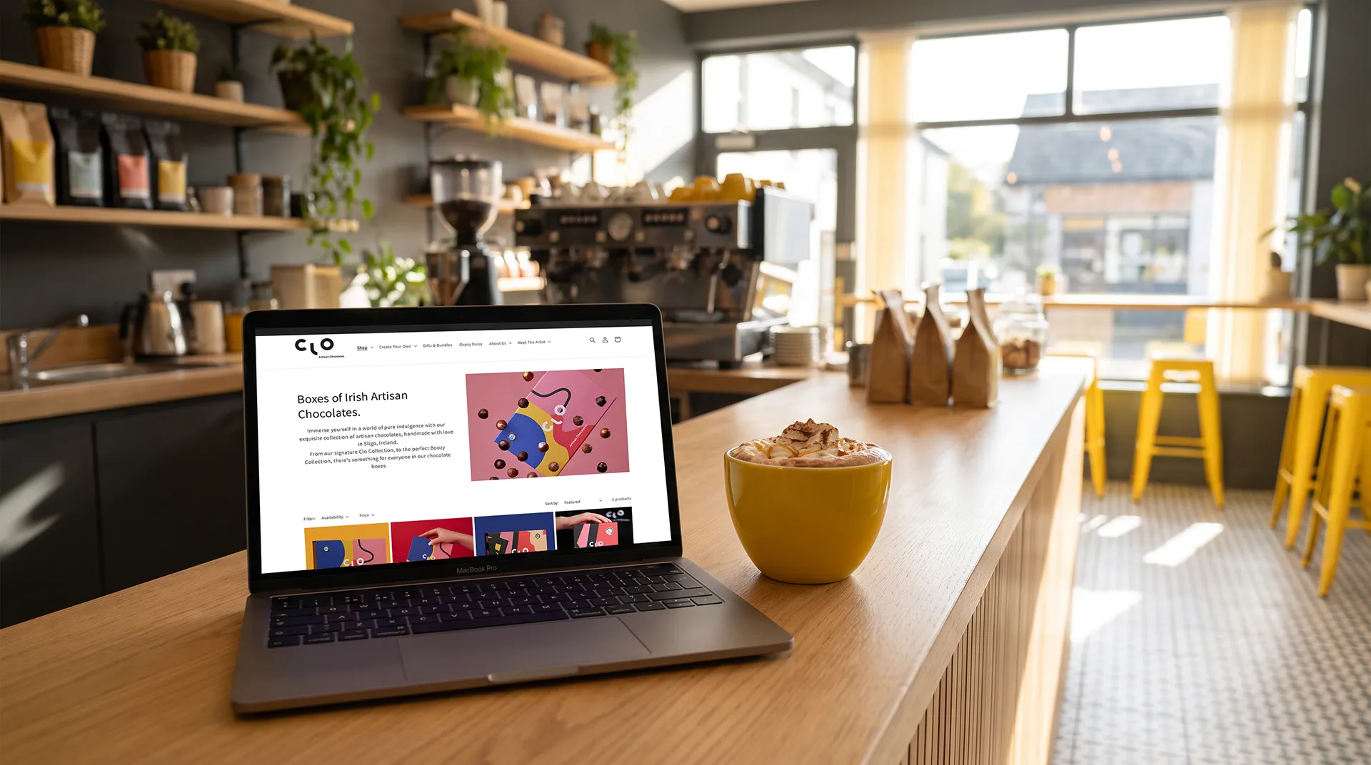 Clo chocolates website imagery shown on a mac book laptop in a cafe with light shining through the window behind.
